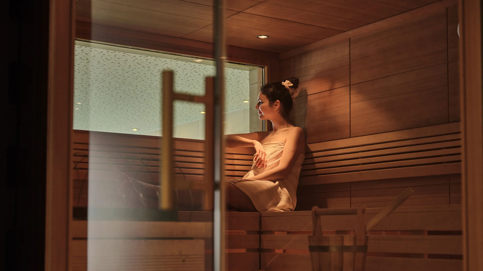Frau entspannt in Sauna, sitzt auf Holzbank mit Handtuch