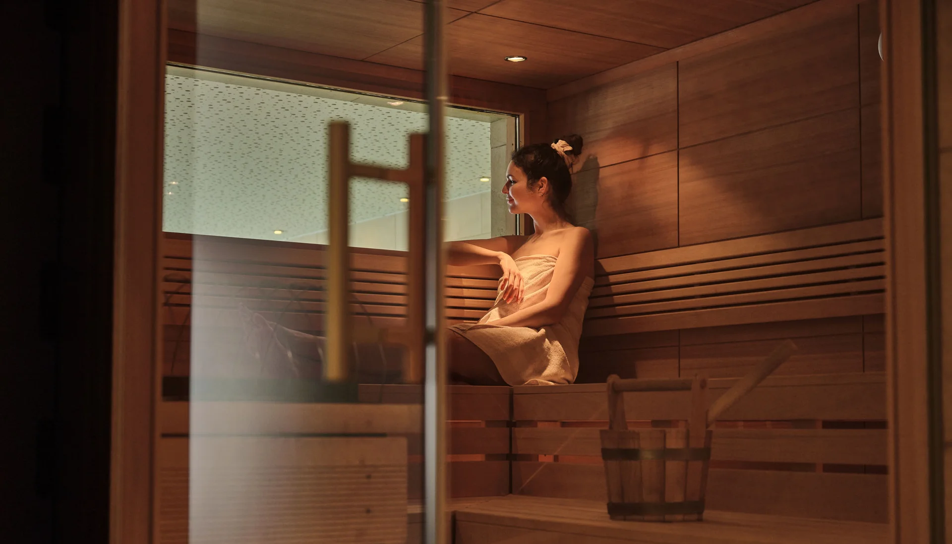 Frau entspannt in Sauna, sitzt auf Holzbank mit Handtuch
