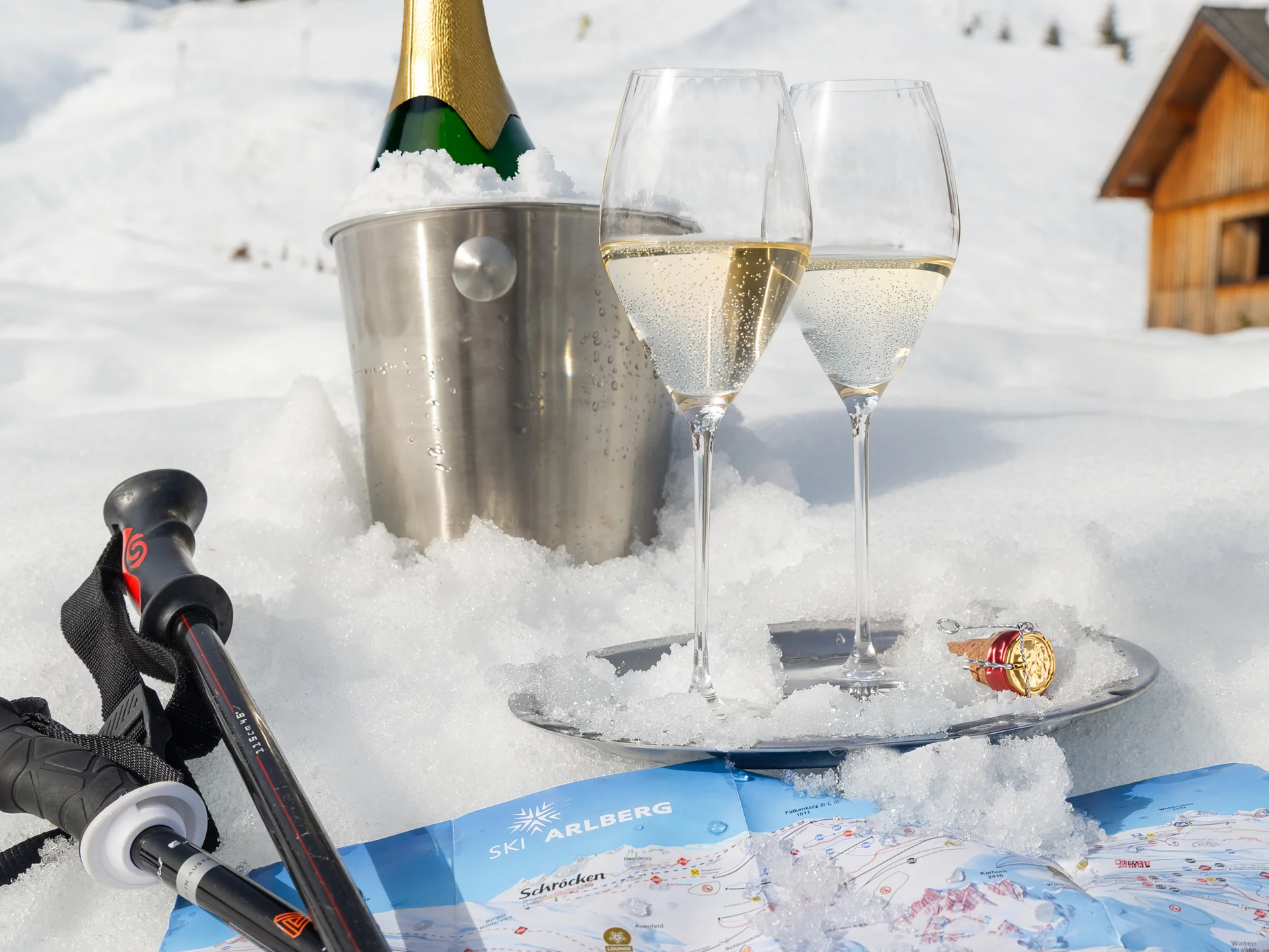Bilder und Impressionen aus dem Sunora Sektflasche im Eiseimer, zwei Gläser, Skistöcke und Ski-Piste Karte im Schnee